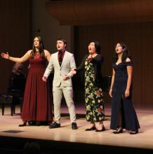 Four student singers singing on stage toward the audience
