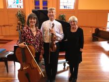 Cellist, violinist, and pianist standing together with their instruments