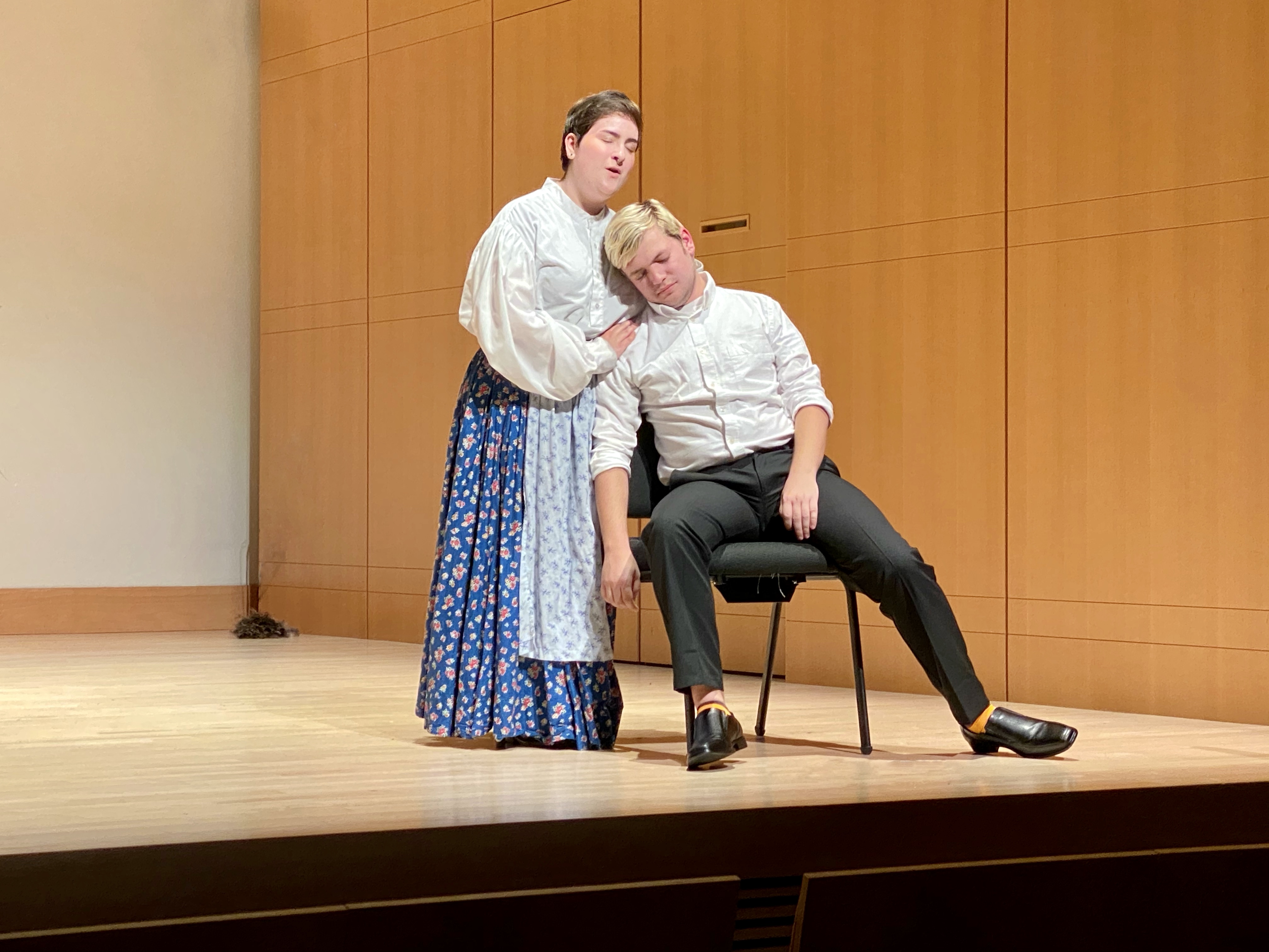 Actor sitting on a chair and leaning against an actress who is standing on stage of Schroeder Hall