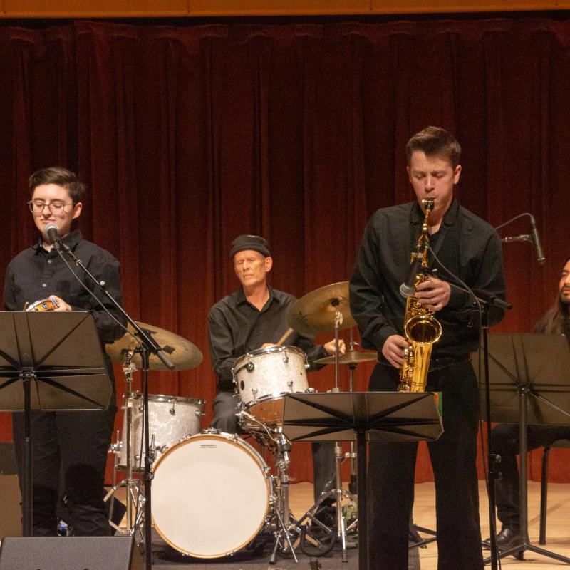 Small jazz combo performing on stage with musicians playing trumpet, saxophone, drums, and bass