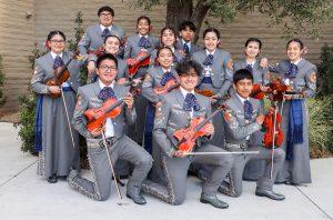 Group of mariachi musicians posing outdoors in traditional matching gray outfits, holding violins and other instruments