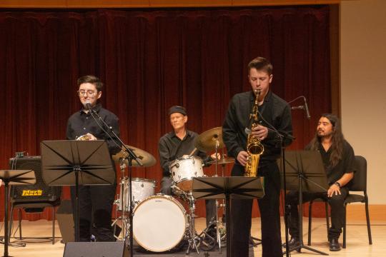 Small jazz combo performing on stage with musicians playing trumpet, saxophone, drums, and bass