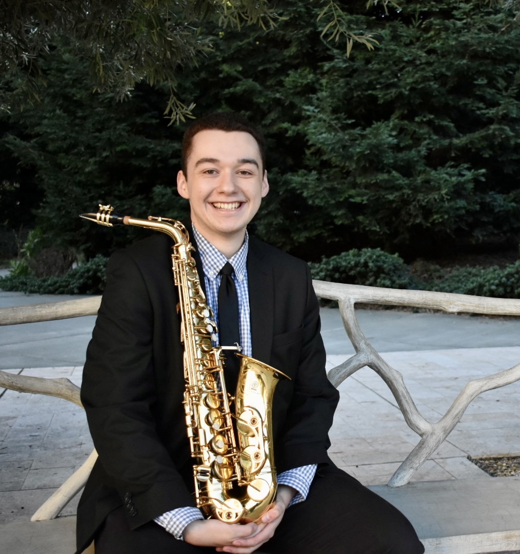 Matthew Bowker headshot holding a saxophone and sitting on a bench outdoors