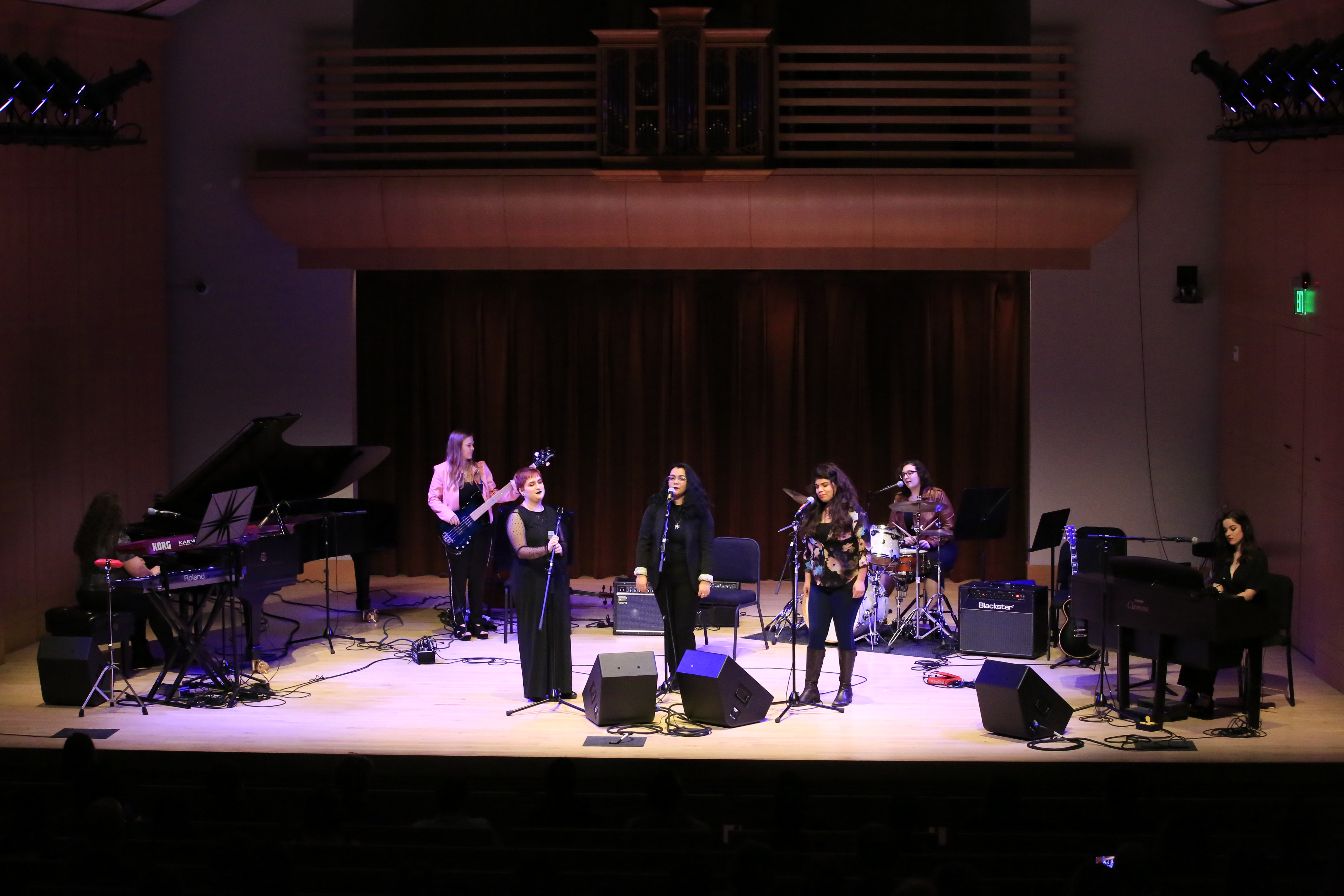 Band of women playing on stage with three singers front and center on Schroeder Hall stage