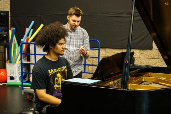 Jomei Greer practicing at piano with instructor behind