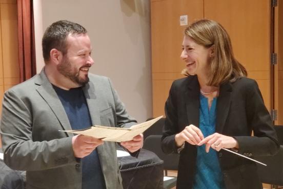 Justin Montigne holding paper and Jenny Bent holding a baton looking at each other and laughing