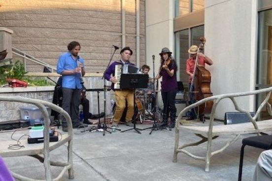 A band playing in the outdoor courtyard of Schroeder hall with benches in front of them
