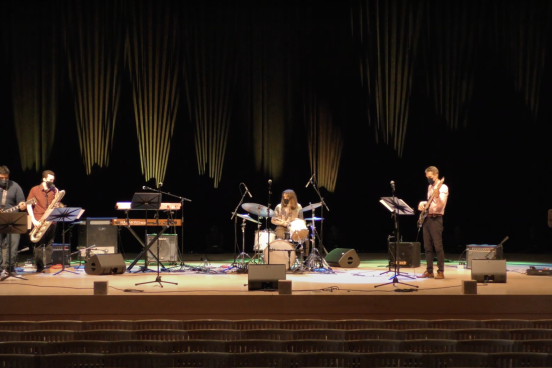 Band playing on stage at Weill Hall with drums, guitars, saxophone, and lighting in the background