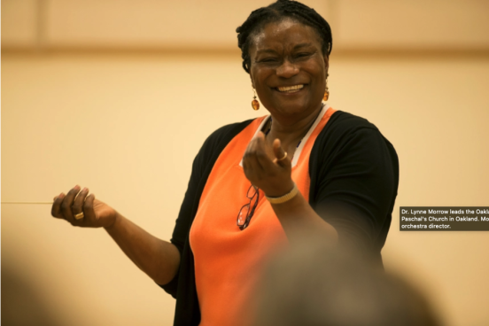 Lynne holding up her hands with baton and smilig 