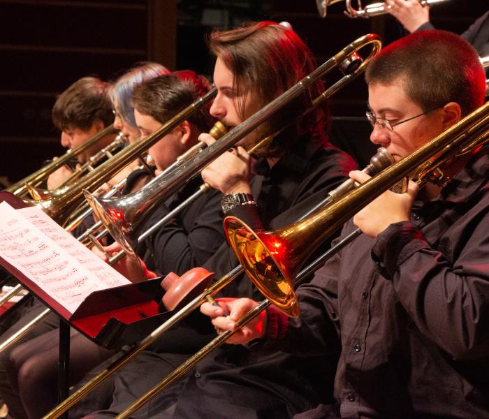 people playing trombone in a row with red light shining on them