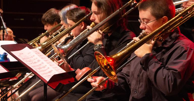 people playing trombone in a row with red light shining on them
