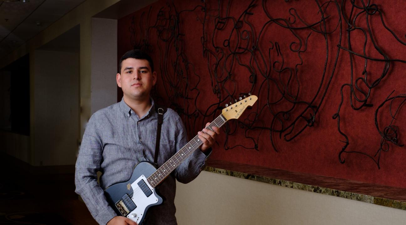 David Lechuga holding electric guitar in front of art in a hallway