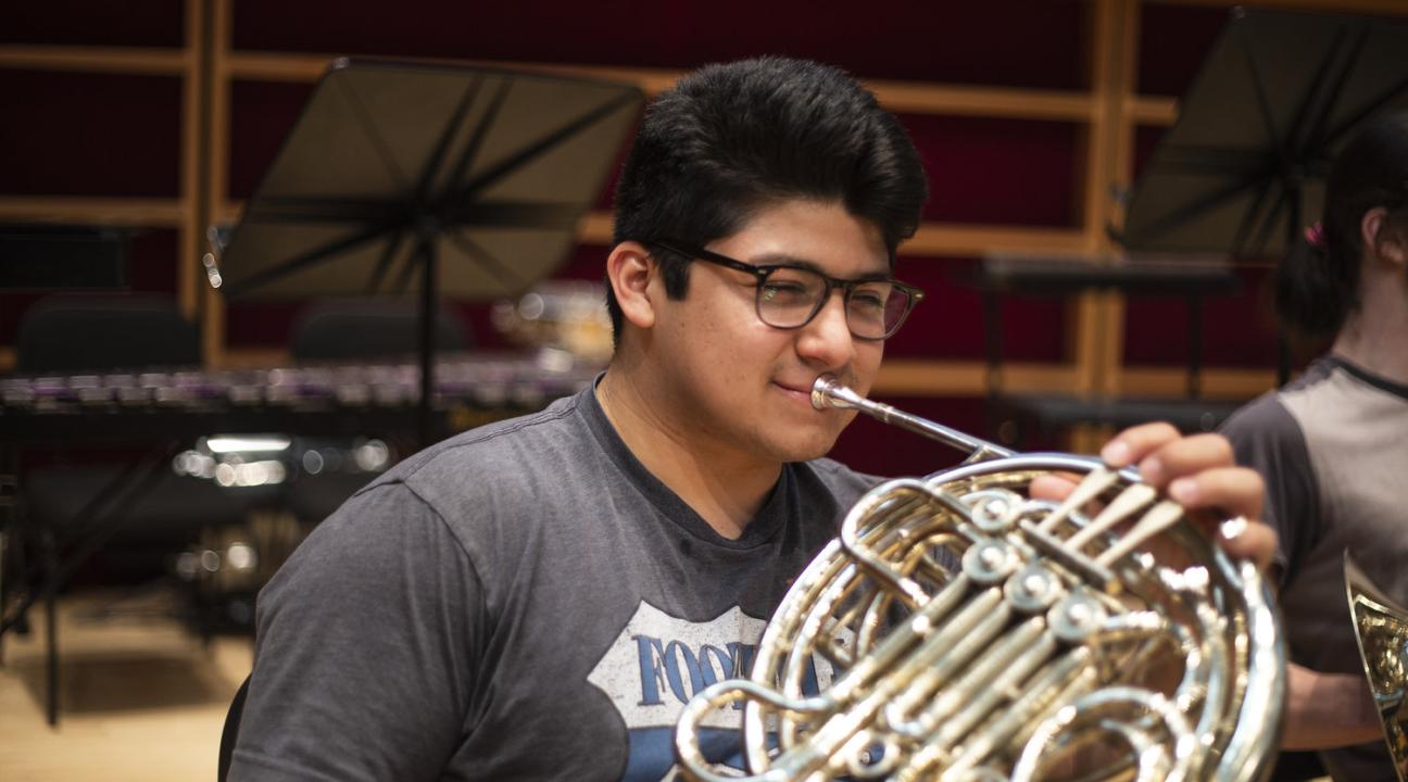 A college student plays the musical instrument, the French horn, during symphony rehearsal