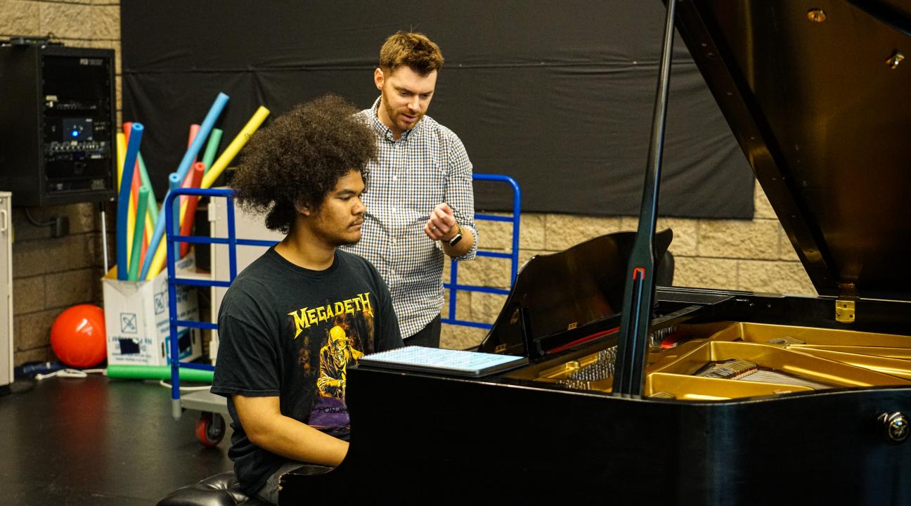 Jomei Greer practicing at piano with instructor behind