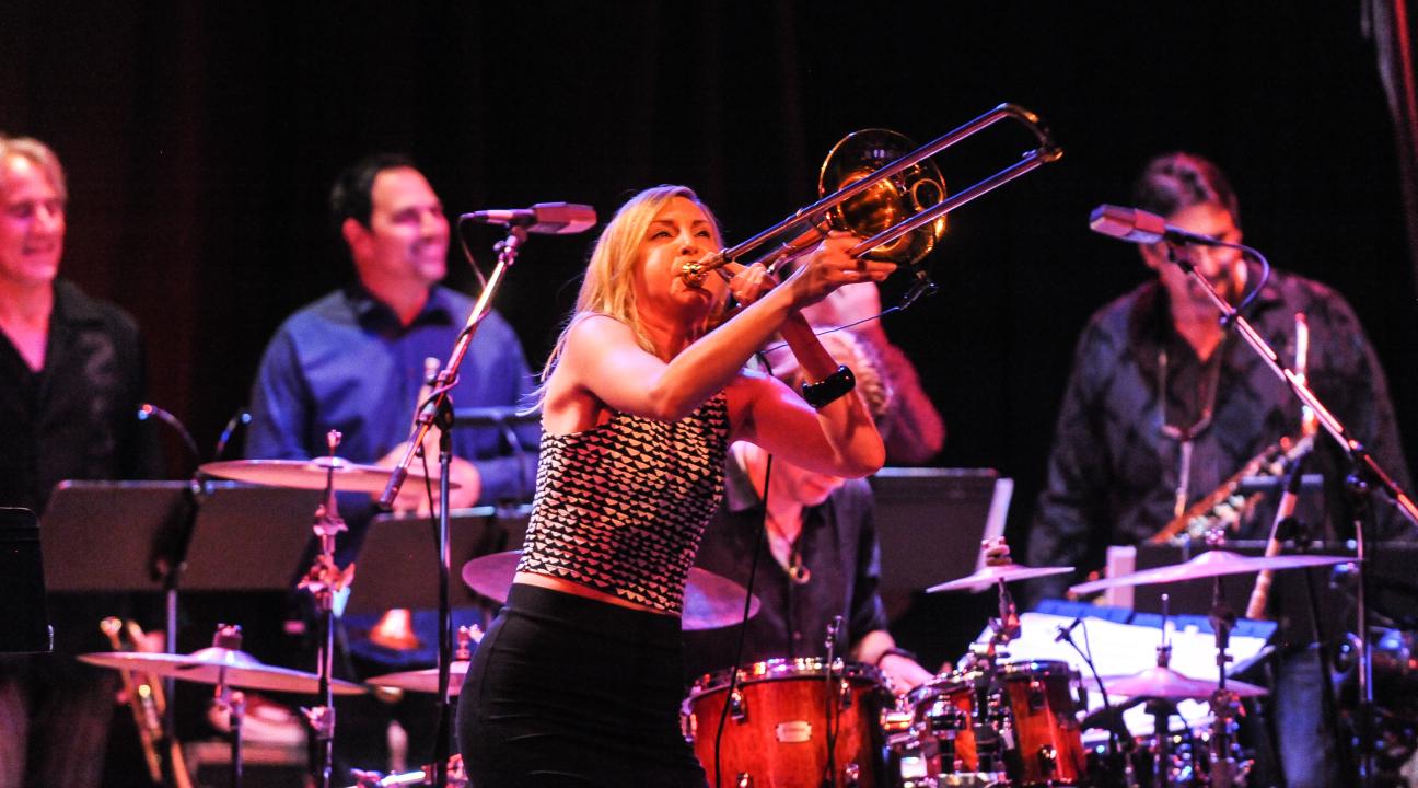 Jeanne Geiger on stage playing trombone with drummers behind her