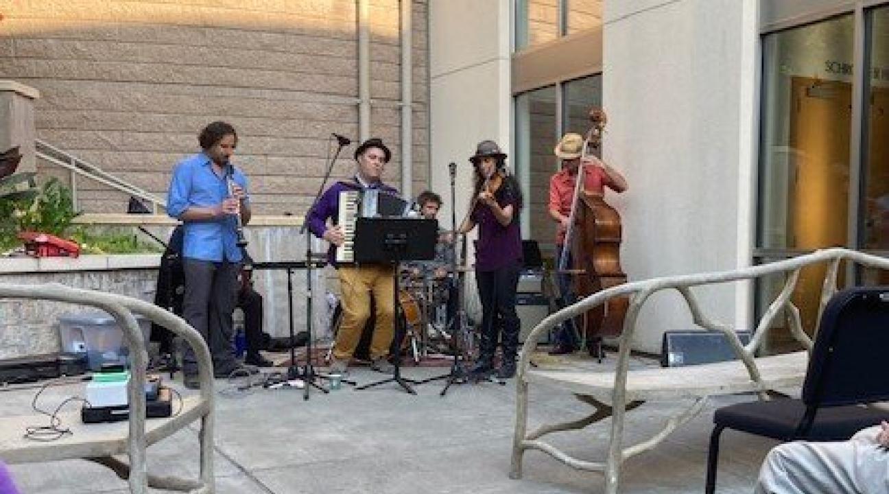 A band playing in the outdoor courtyard of Schroeder hall with benches in front of them