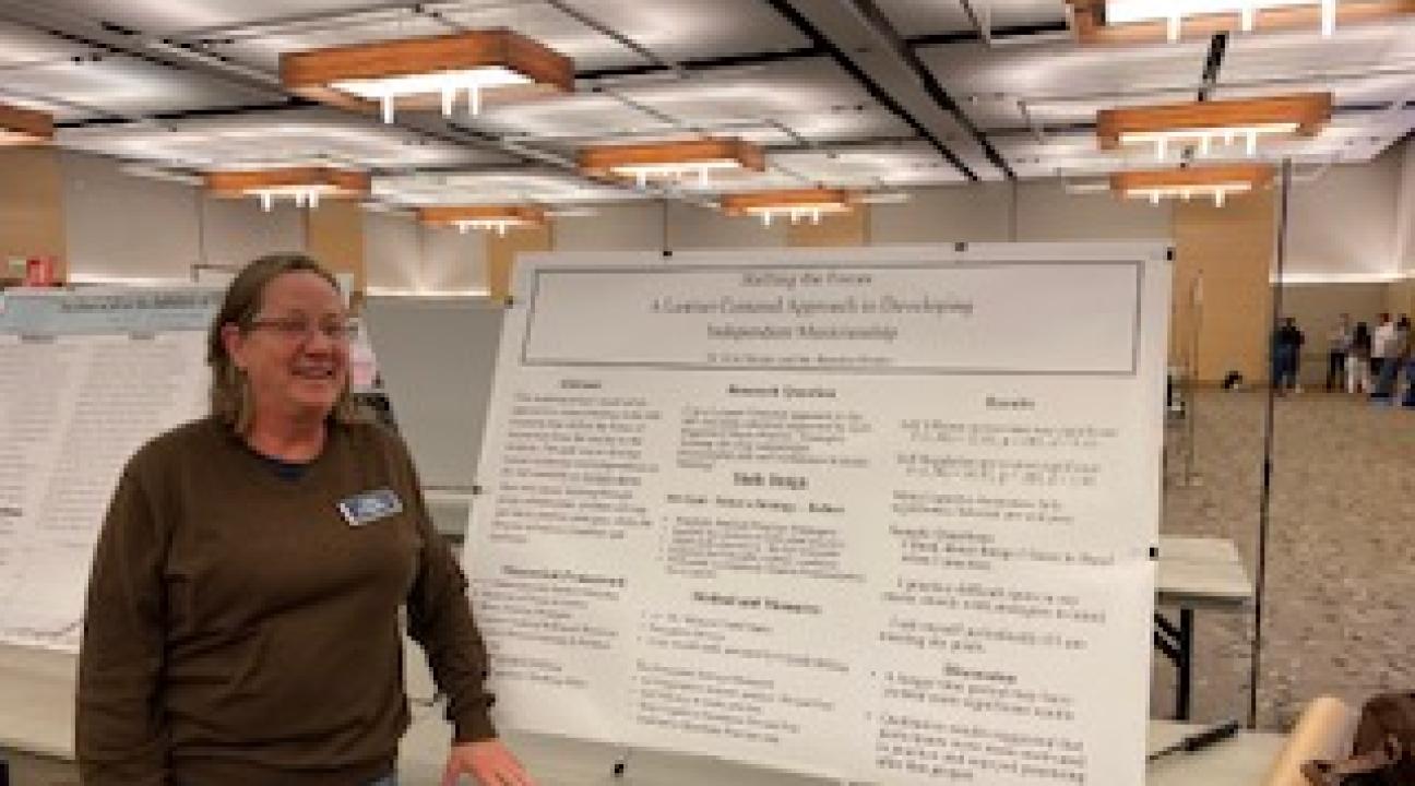 Dr Mieder standing in front of a poster board on a table in the student center ballroom