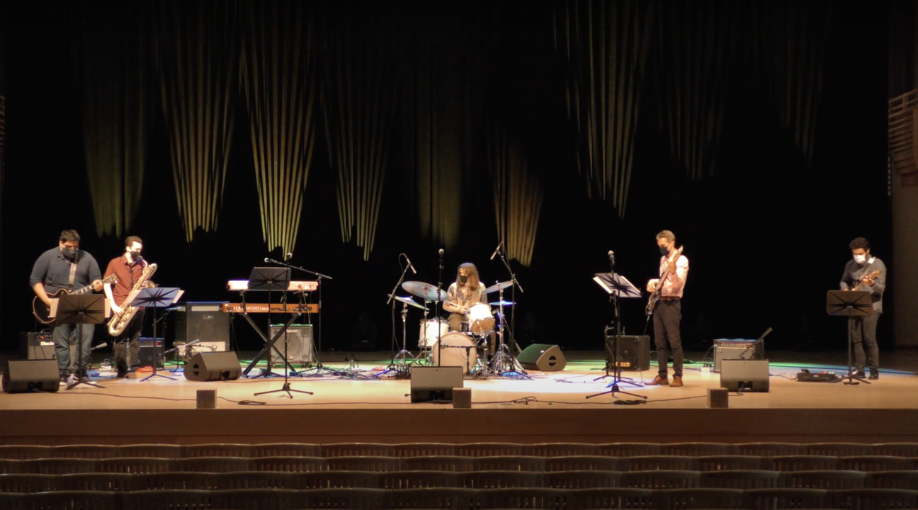 Band playing on stage at Weill Hall with drums, guitars, saxophone, and lighting in the background