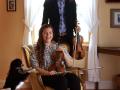 Aaron Westman holding violin standing behind Anna Washburn sitting and holding violin with their dog
