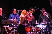Jeanne Geiger on stage playing trombone with drummers behind her