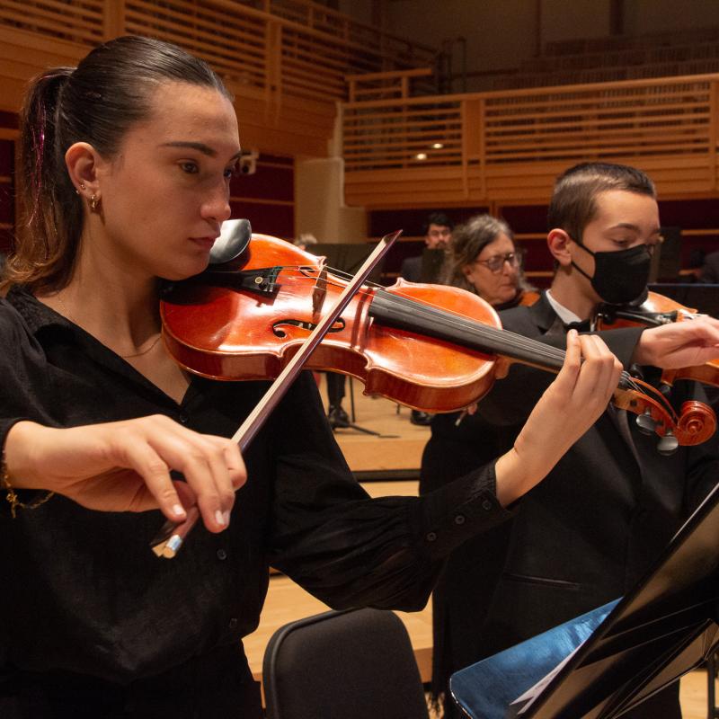 Two violinists with one wearing a mask