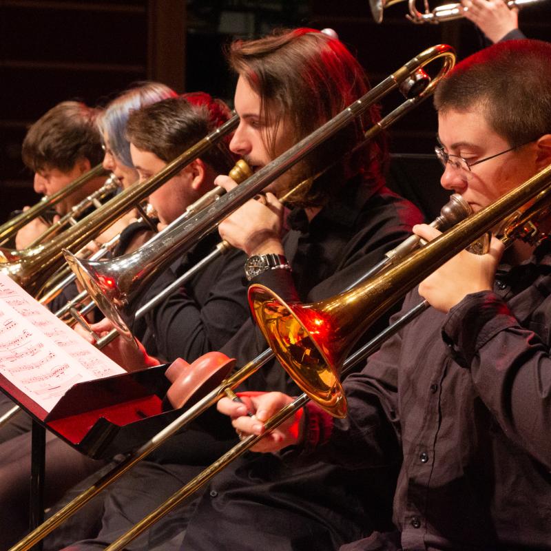 people playing trombone in a row with red light shining on them