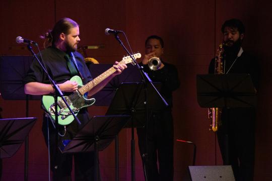 Guitarist with brass players in the background