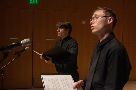 Two singers with binders singing on stage