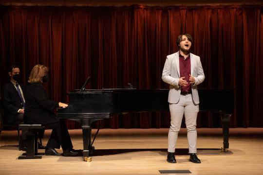 Student singing in front of a piano on stage