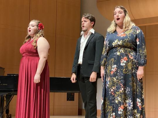 Three singers on stage with a piano in the background