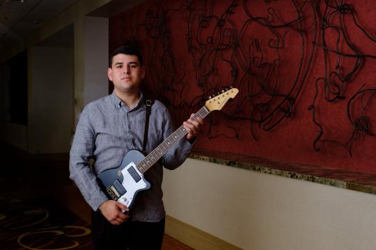 David Lechuga holding electric guitar in front of art in a hallway