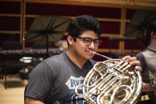 A college student plays the musical instrument, the French horn, during symphony rehearsal