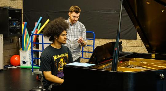 Jomei Greer practicing at piano with instructor behind