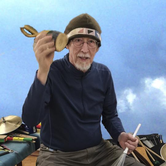 George Marsh holding a maraca and playing the drums with a blue background