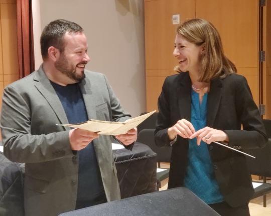 Justin Montigne holding paper and Jenny Bent holding a baton looking at each other and laughing