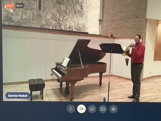 man playing french horn with a music stand and standing next to a piano