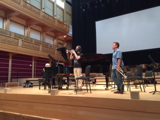 Mark Inouye on Weill Stage holding a trumpet and watching Hikaru Hallberg playing the trumpet beside him with Marilyn Thompson playing piano