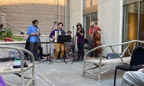 A band playing in the outdoor courtyard of Schroeder hall with benches in front of them