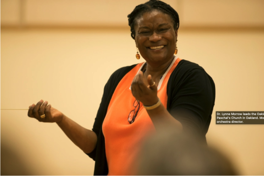 Lynne holding up her hands with baton and smilig 