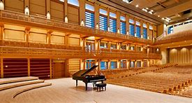 A piano on the stage, surrounded by a beautiful and empty concert hall is ready for the evening's performance.