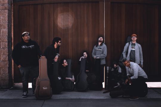 Guitarists standing/kneeling by a wooden gate