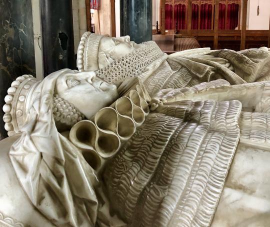 A picture of a couple as marble figures on their crypt.