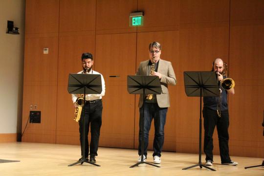 two saxophones players and a trombone player with music stands