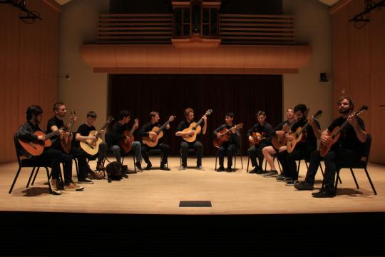 Guitarists with their guitars on stage sitting in a curved line