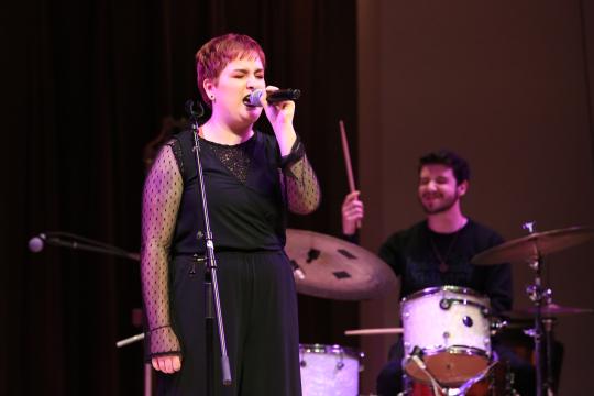 Singer with a microphone left, drummer at a drum kit with his stick raised on the right