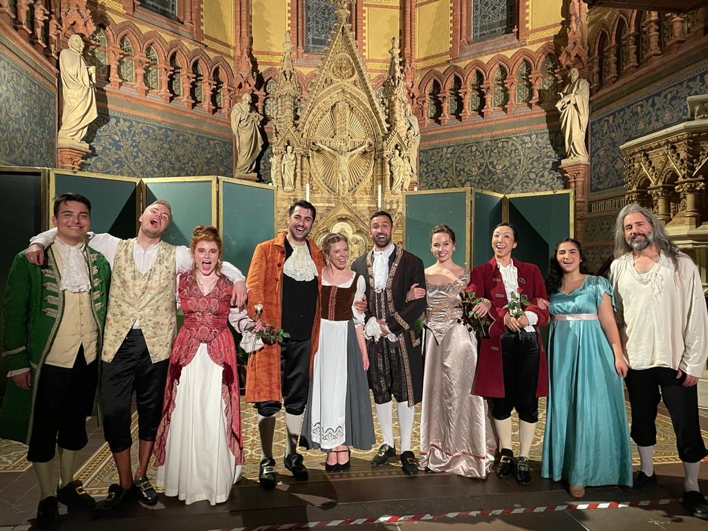 Ensemble of opera singers standing for a group photo inside a cathedral